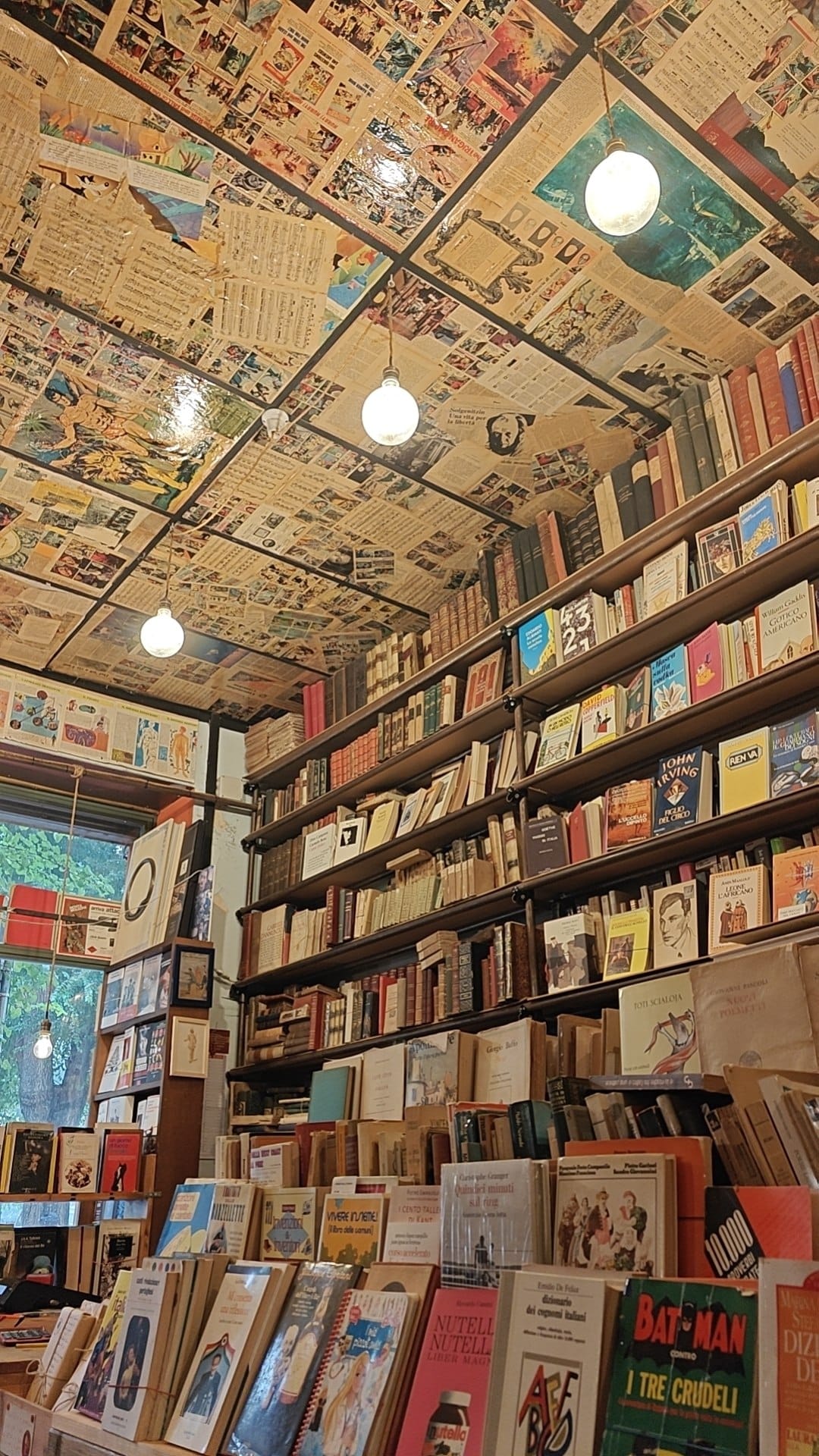 L'interno della libreria: scaffali carichi di libri fino al soffitto e due lampade appese.