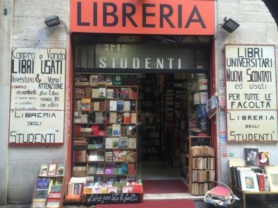 La facciata della libreria: l'insegna LIBRERIA, la vetrina piena di libri e i due cartelli dipinti ai lati della porta.